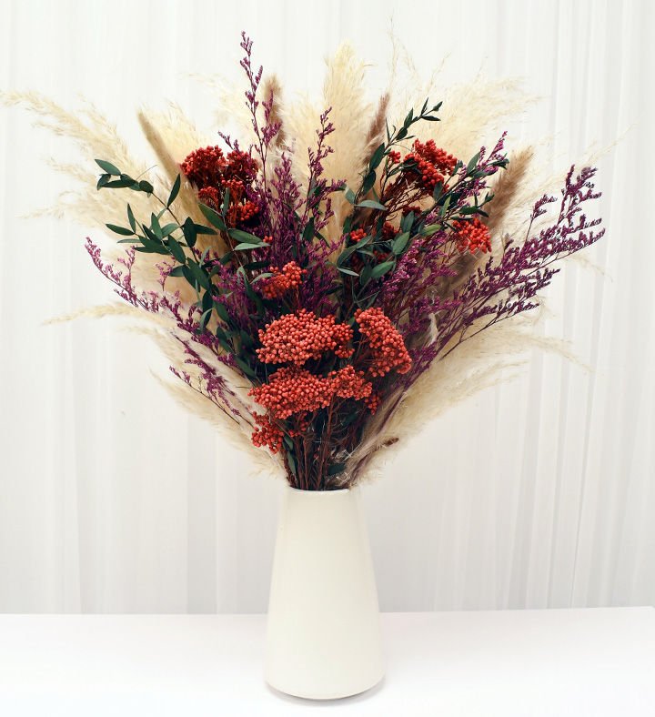 Colorful dried flower bouquet with pampas, greenery, and berry-toned accents in a white vase