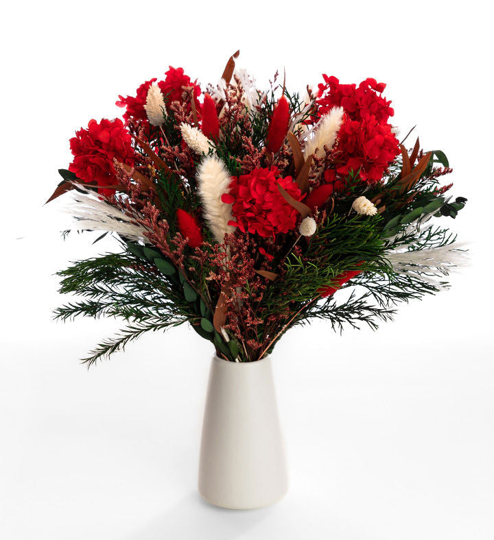 Jolly Holiday dried bouquet with red hydrangea, white plumes and green foliage in a tapered ivory vase